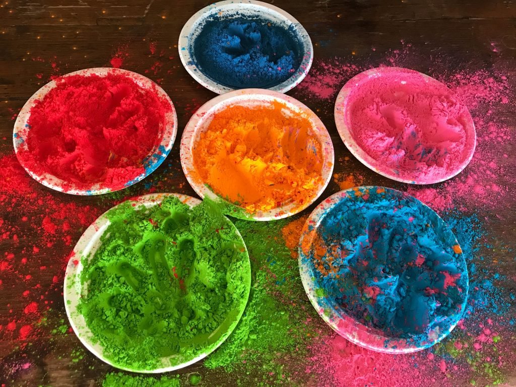 Colorful Holi powders on plates, showcasing vibrant hues on a rustic wooden background.