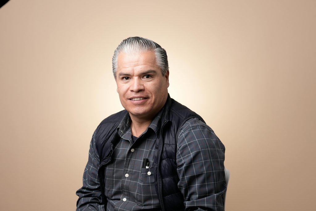 Mature man with stylish hair poses confidently in a studio setting against a neutral background.