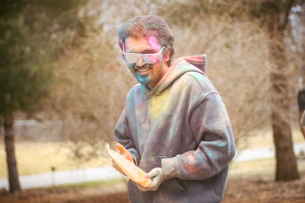 Happy man covered in colorful powders during outdoor Holi festival celebration.