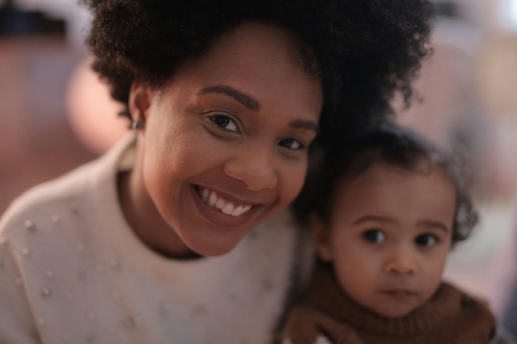 A cheerful mother embracing her toddler indoors, both smiling warmly.
