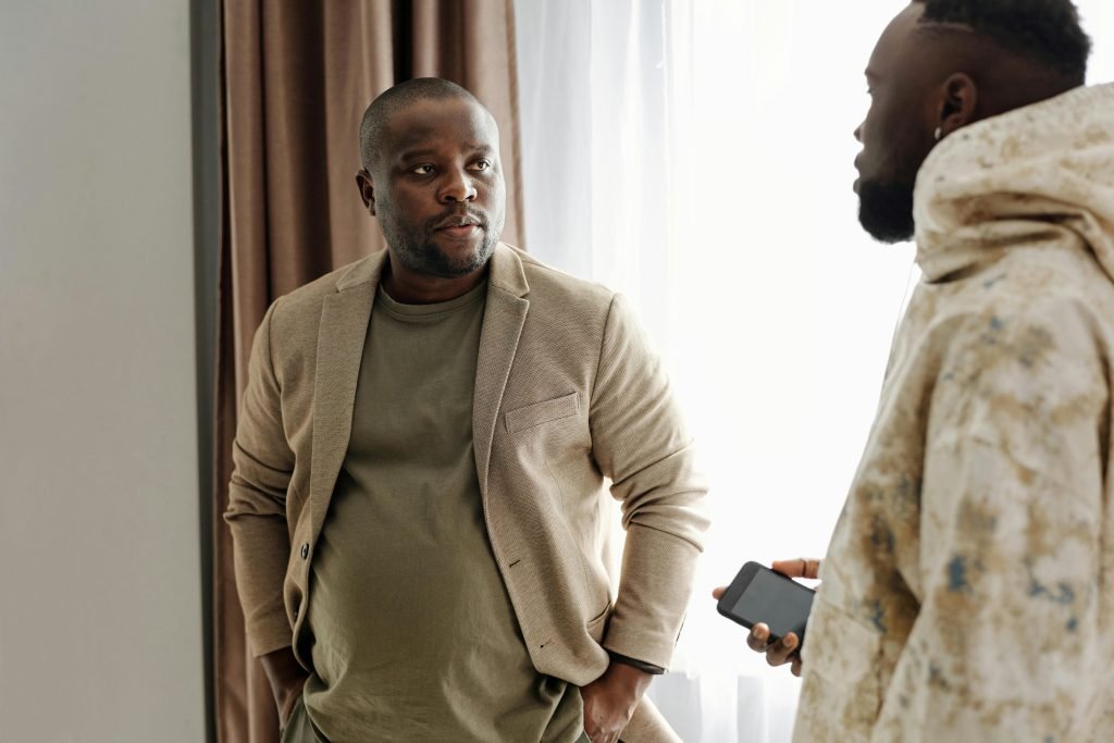 Two men engaged in a serious conversation indoors, one holding a smartphone.