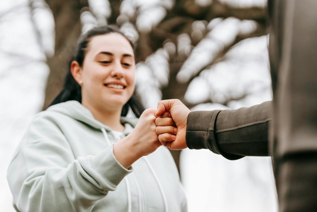 Two friends in casual wear sharing a fist bump outdoors, expressing friendliness and positivity.