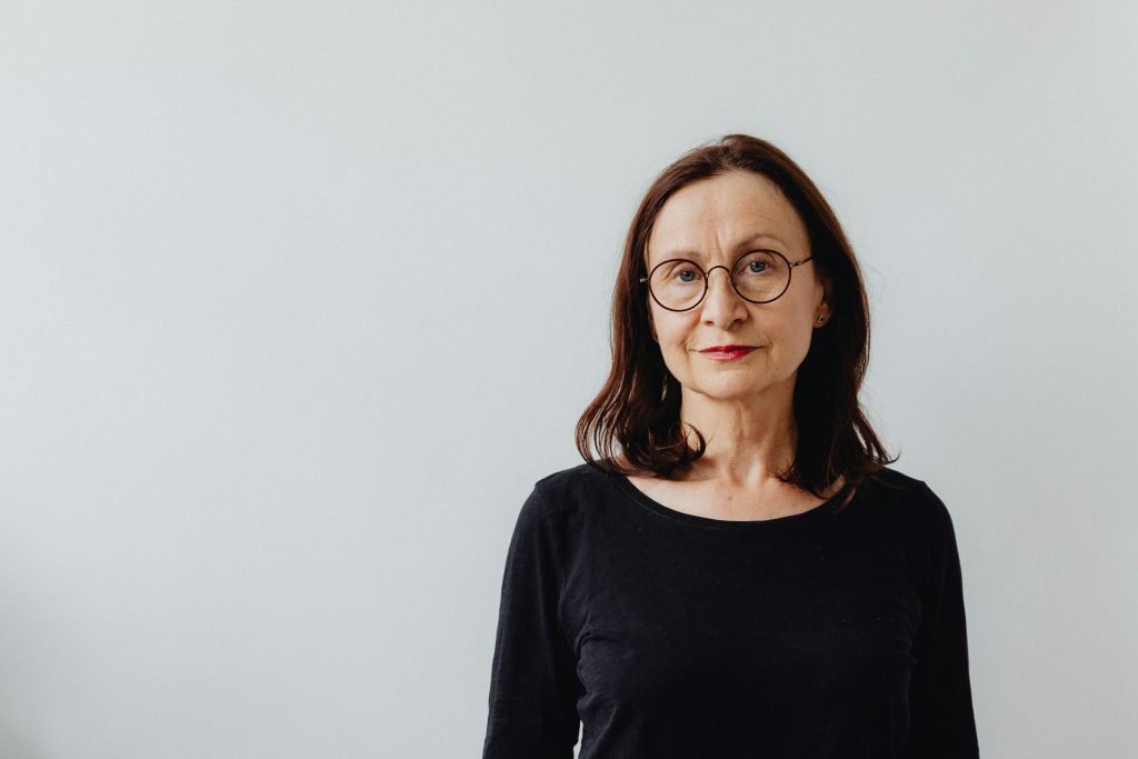 Elegant portrait of a mature woman in black shirt with eyeglasses on white background.